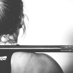 Une femme de dos qui porte une barre d'haltères au niveau des épauules.